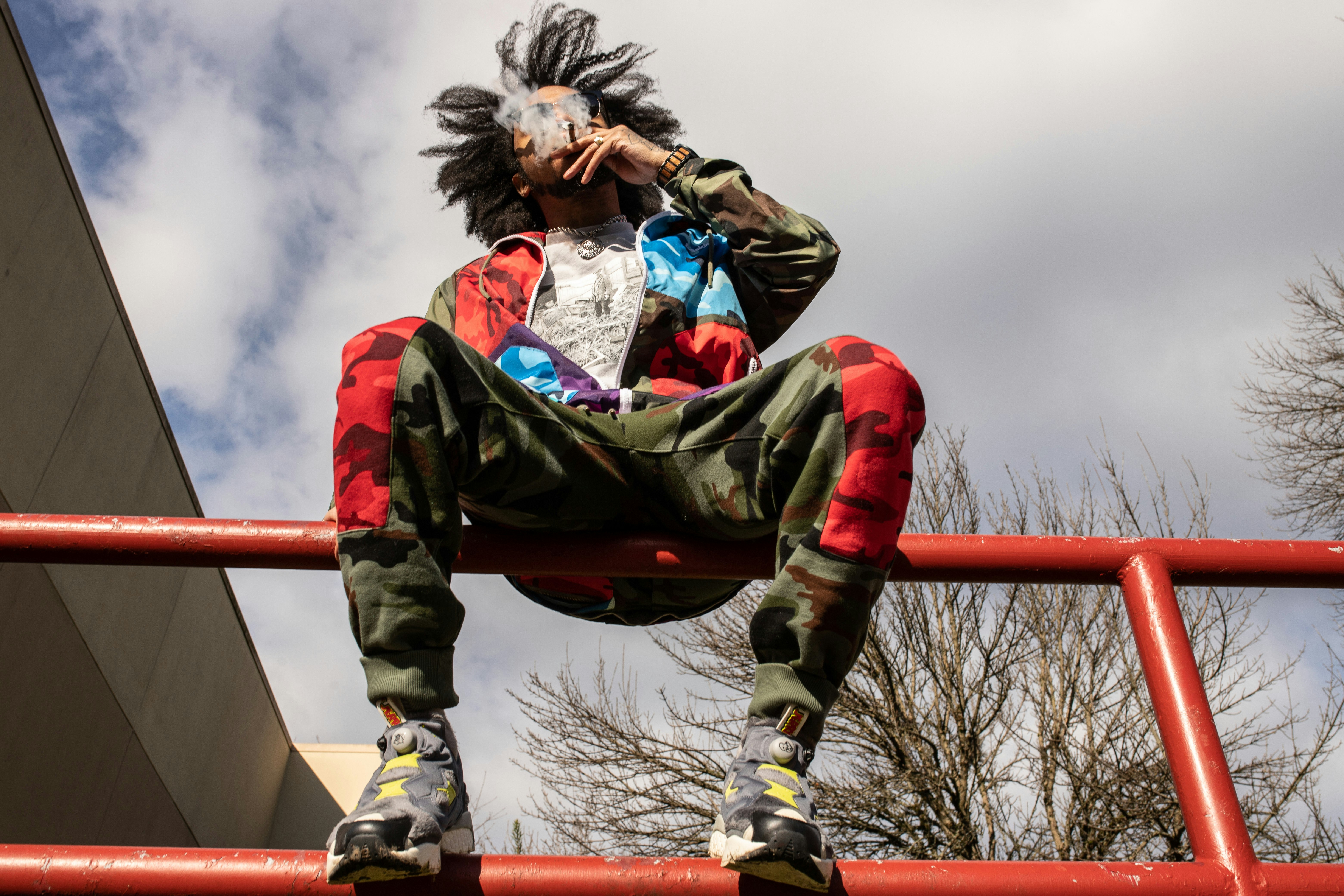 man in green jacket and blue denim jeans sitting on red metal bar during daytime